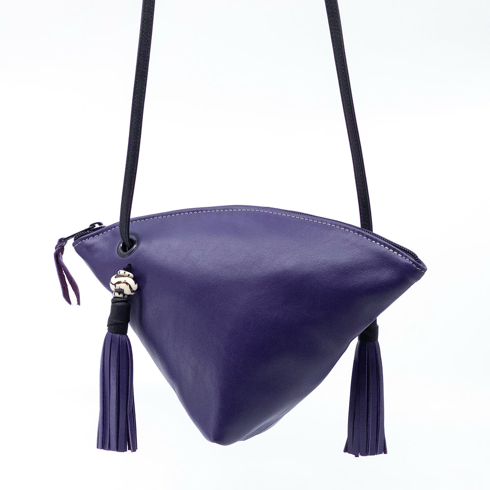 A purple triangular leather crossbody bag with a black strap, matching purple tassel zipper pull, and tassel details, shown against a plain white background.